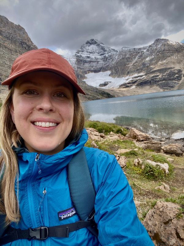 Wren taking a selfie at McArthur Lake, BC. She is smiling and wearing a red baseball hat and blue jacket